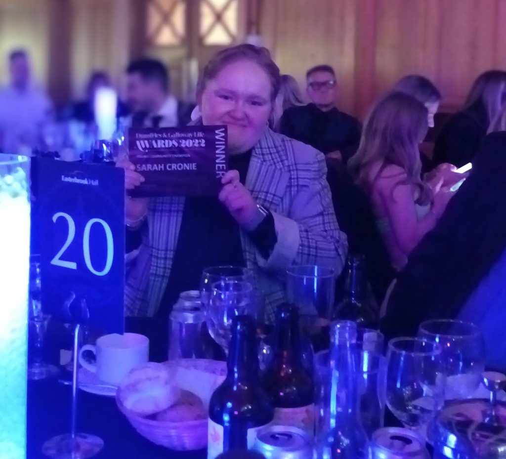 Young woman at awards dinner table holding up winners certificate