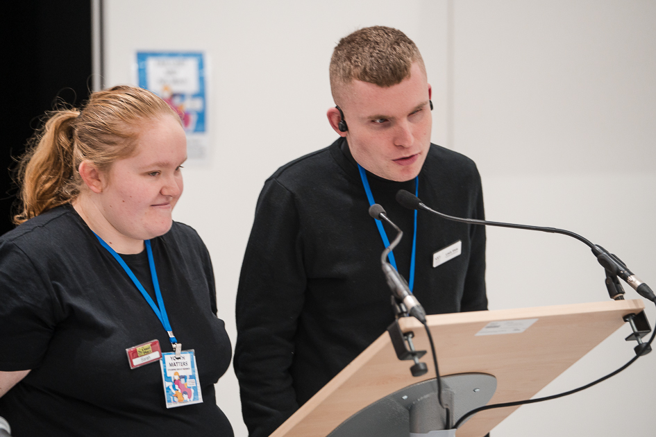 Photo of Sarah Cronie and Lewis Shaw speaking at lecturn with microphones addressing the Youth Matters conference
