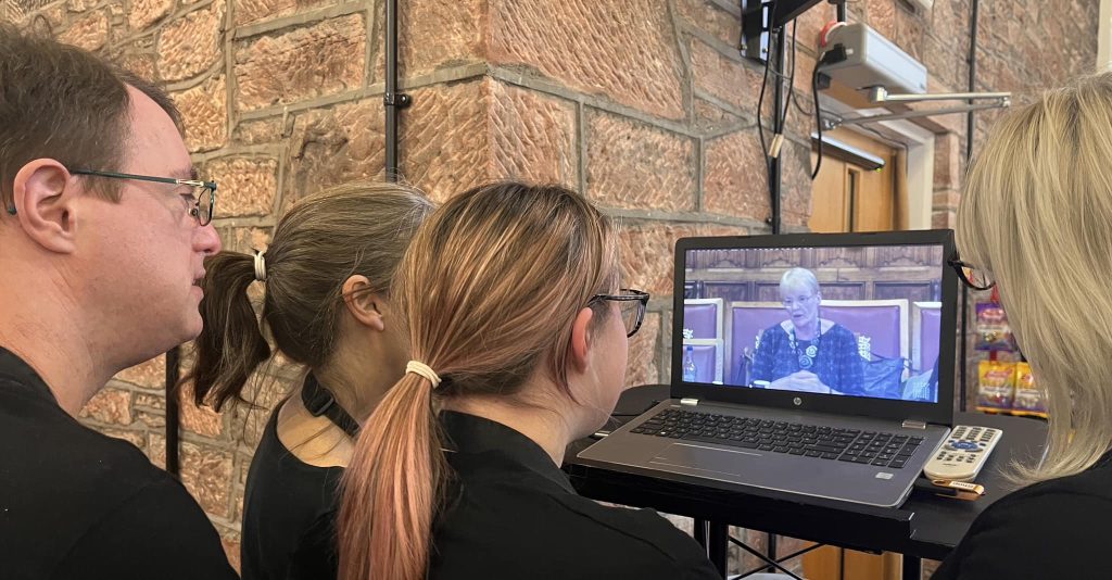 young people look on as a woman is speaking on a screen in house of lords
