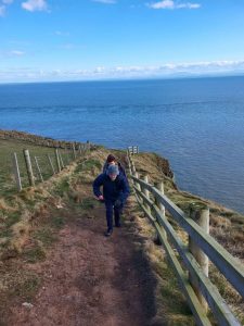 People walking up a steep cliff top with sea behind them and fences on either side