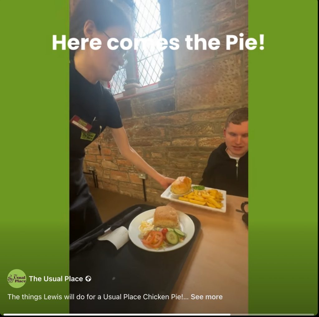 Young man sits at a table and smiles as a young server brings him a large pie and chips