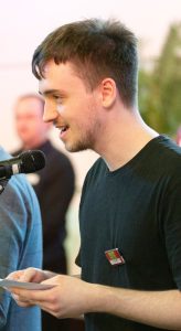 Young Man is smiling and speaking into a microphone, He has short dark hair