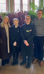 Two volunteers stand centre of the photo wearing The Usual Place uniform. On both sides of them are two team members from Farries Kirk & McVean who are wearing casual professional clothes. They are all looking into the camera and smiling.