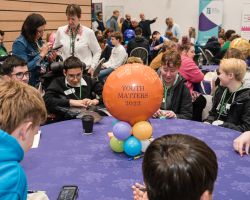 photo at Youth Matters conference looking from behind a circular table with youth matters balloon in the centre and young people around it looking engaged in the speaking