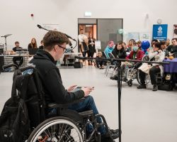photo of Finlay Anderson MSYP in a wheelchair with microphone speaking to full hall of people at conference