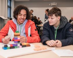 photo of two teen-aged boys sitting at a table smiling with a colourful lego model in front of them