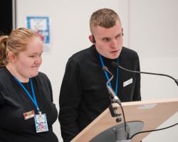 photo of Sarah and Lewis speaking with a lecturn and microphones