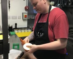 Young man in red tshirt and black 1610 apron peels onions in kitchen