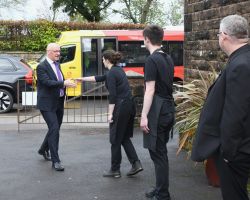 First Minister of Scotland walks towards The Usual Place and is greeted by young woman with outstretched hand. Behind her a young man in Usual Place uniform is waiting to greet him too