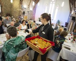 The bread course is served. A young waitress holds a large basket filled with perfectly formed pieces of bread and moves between the guests at tables to serve the fresh baked items.