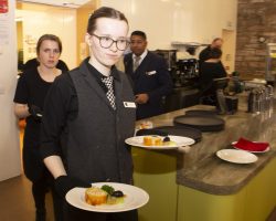 Here comes the starter! Two young women leave the kitchen carrying plates of exquisitely presented food. Behind them the Hospitality Manager watches and encourages.