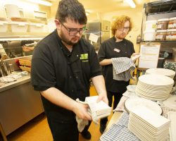 Two men are stacking plates and drying them as they leave the dishwasher.