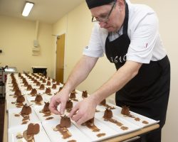 An experienced chef checks and adds finishing touches to long rows of plates with chocolate desserts.