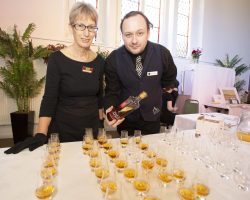 Annandale Whisky anyone? Bar manager and waitress stand beind a table with rows of whisky tasting glasses filled with a golden liquid. They hold a bottle of Annandale Distillery Whisky