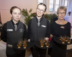 Whisky Toast Three waitresses stand holding trays of whisky in glasses.
