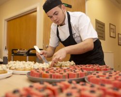 Chef Sam ensures each canape is perfectly presented Young chef stands behind a table covered in plates of beautiful small canapes. He is working on them.