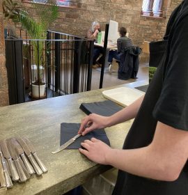 A volunteer neatly wrapping a black napkin around a knife on the counter.