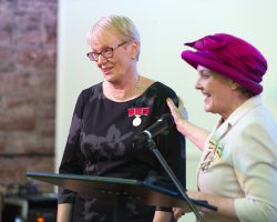Heather Hall BEM and Fiona Armstrong, Lord Lieutenant of Dumfries.  Image Allan DevlinTwo ladies stand behind a lecturn with a microphone. They are both w=smiling towards the audience. Each is smartly dressed and each has an Honour Medal with ribbon pinned to their dress/jacket.